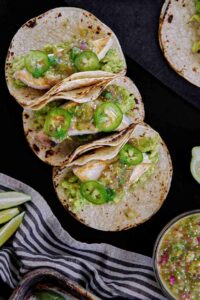 Three tacos topped with green salsa.