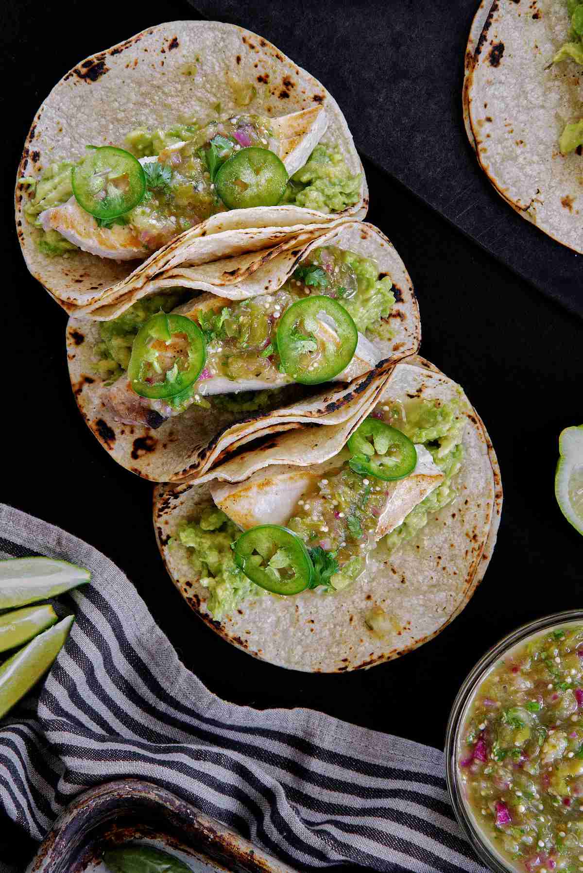 Three tacos with green salsa on a black table.