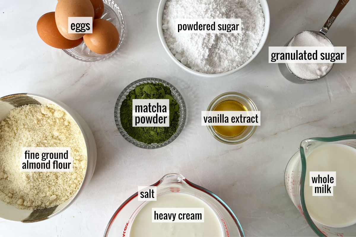 Sugar, eggs, green tea powder, and other ingredients on a white countertop.