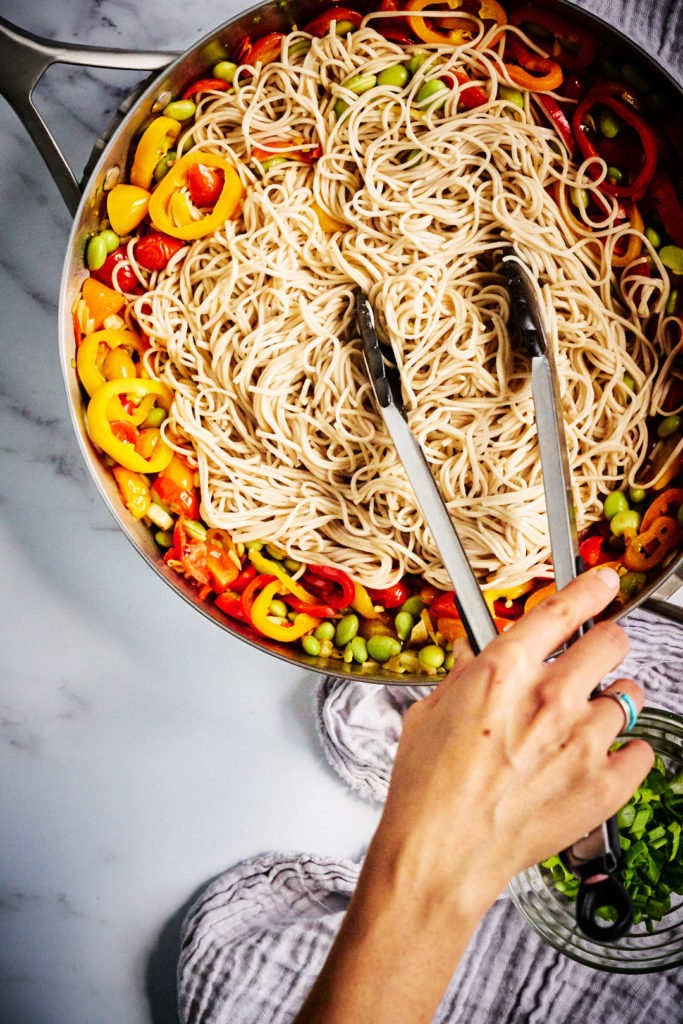 Tongs mixing noodles into a stir fry.