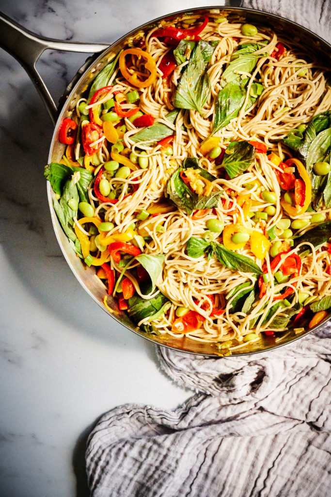 Noodle stir fry in a pan with fresh basil.