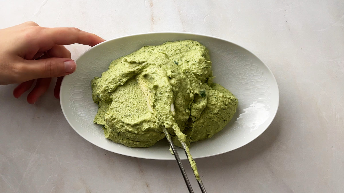 Green hummus on a white, oval plate.