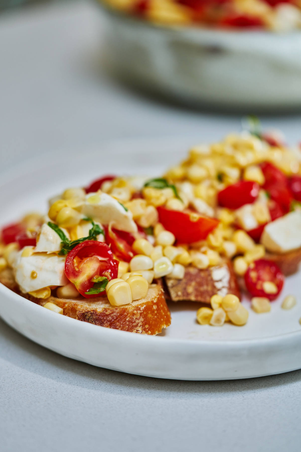 Corn and tomato salad on top of slices of baguette on a white plate.