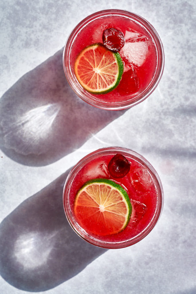 Two red cocktails with lime and cherry with shadows.