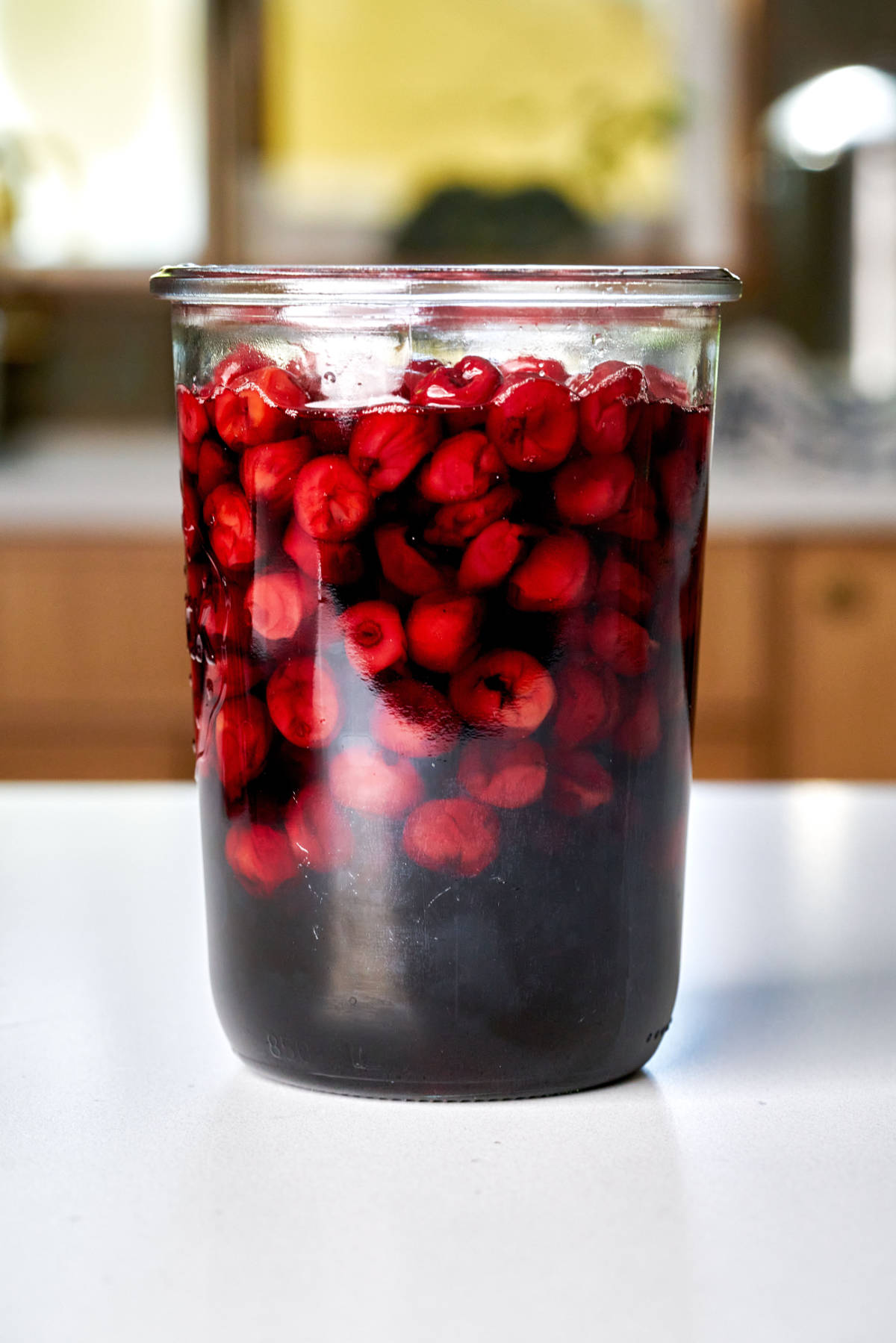 Large jar filled with cherries and dark syrup.