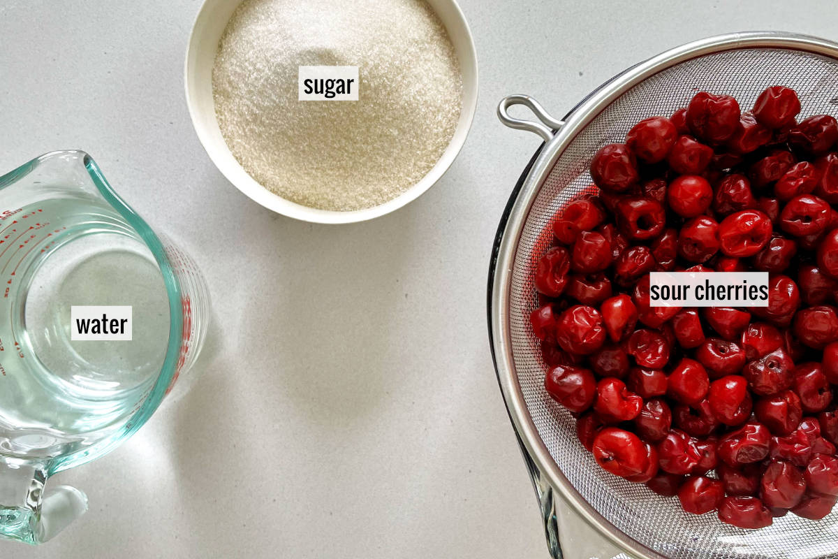 Sour cherries, sugar, and water on a white countertop.