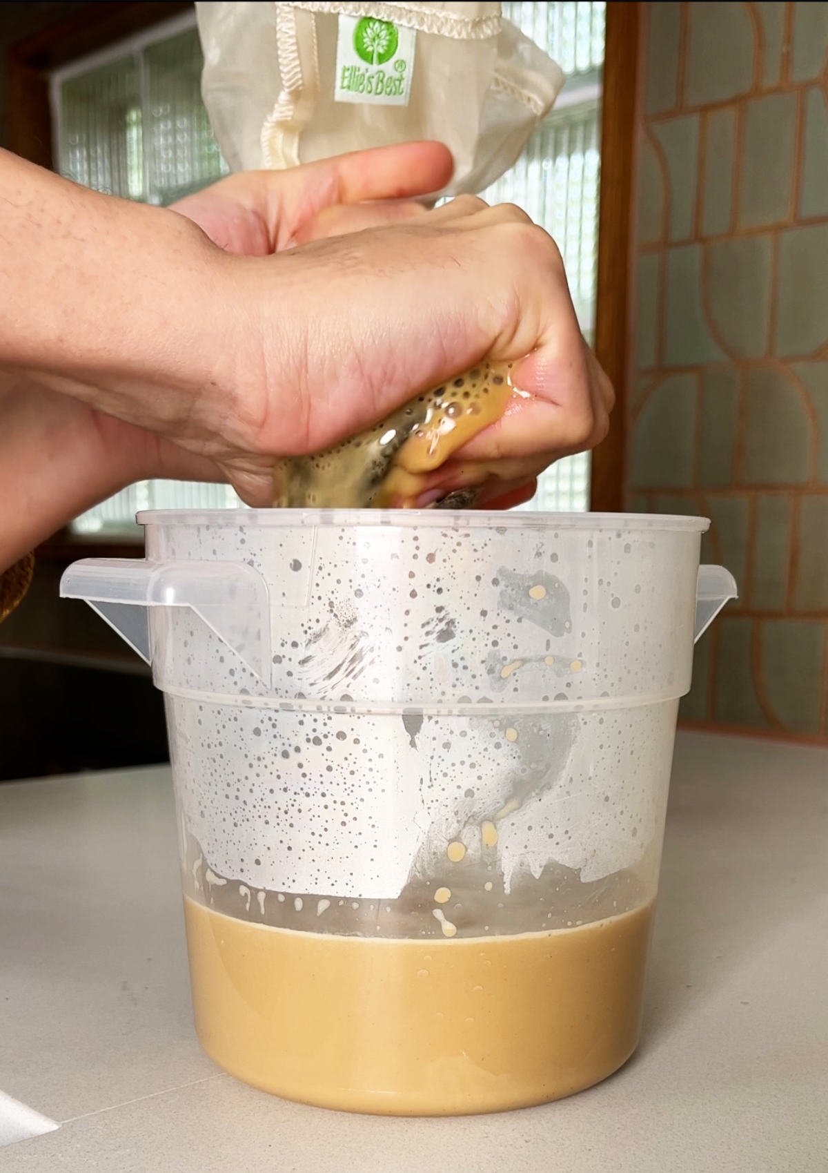 Squeezing liquid out of a nut milk bag into a plastic container.