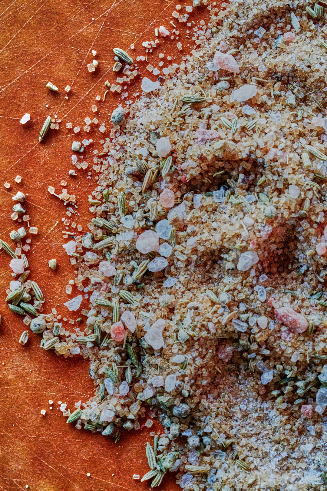 A mixture of sugar, salt, fennel, and white pepper on a red-brown cutting board.