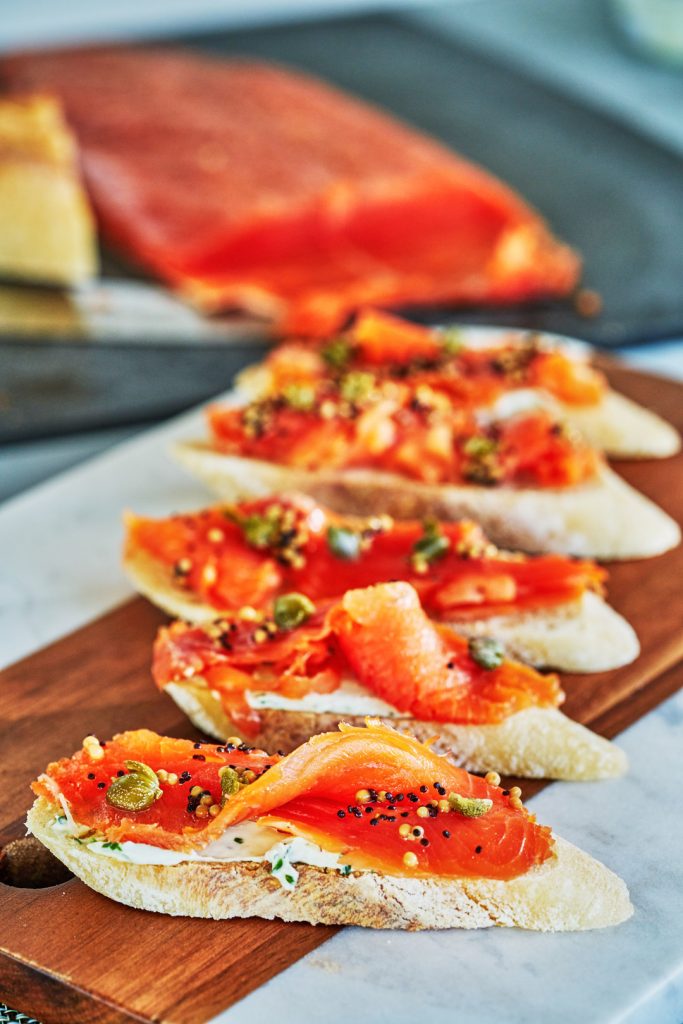 Slices of bread arranged diagonally on a cutting board, topped with cream cheese and cured salmon.