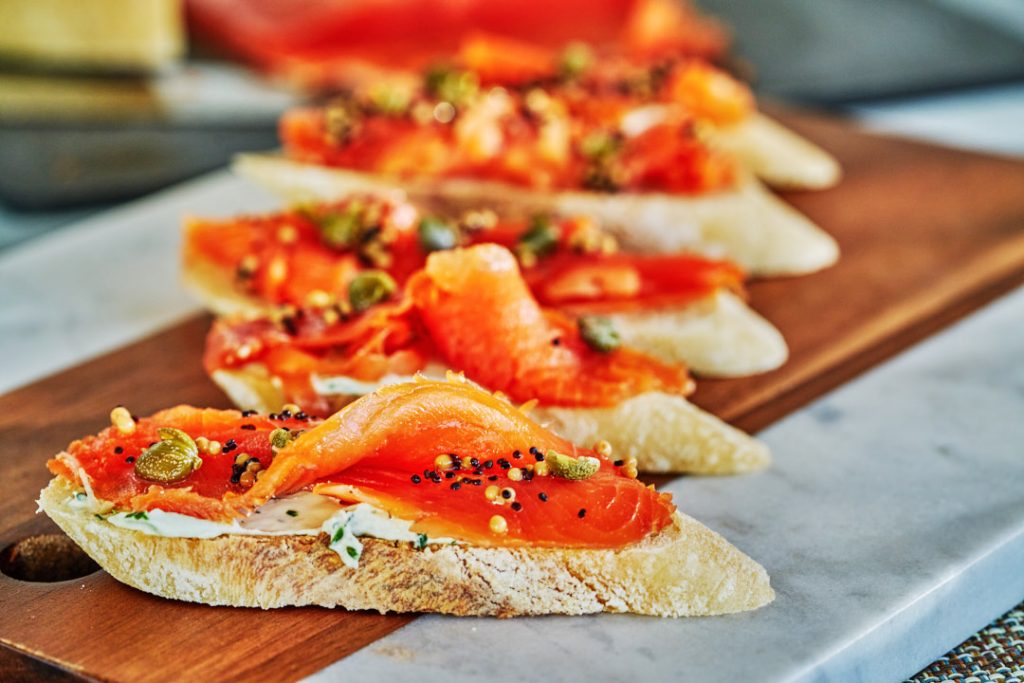 Slices of bread arranged diagonally on a cutting board, topped with cream cheese and cured salmon.