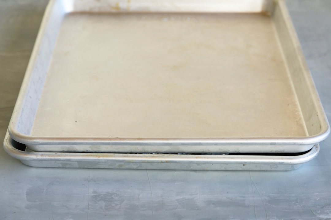 Two large silver sheet pans stacked on top of one another.