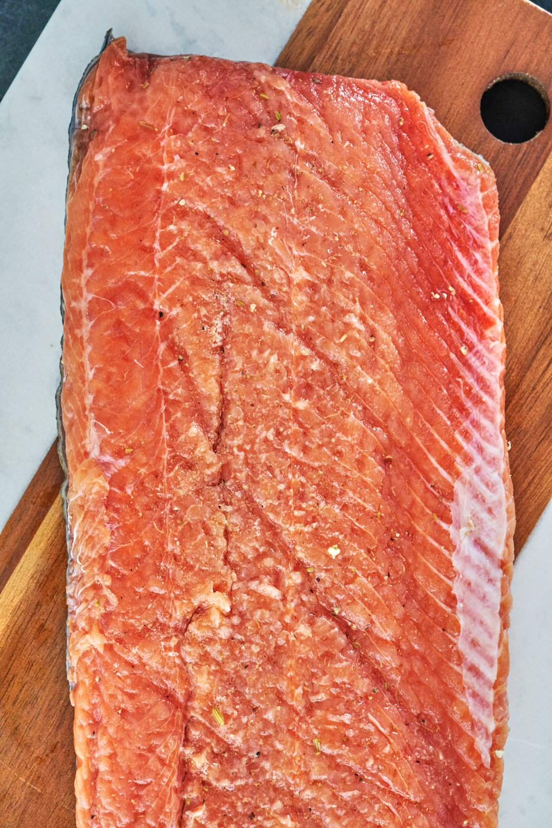 A large piece of salmon on a marble and wood cutting board.