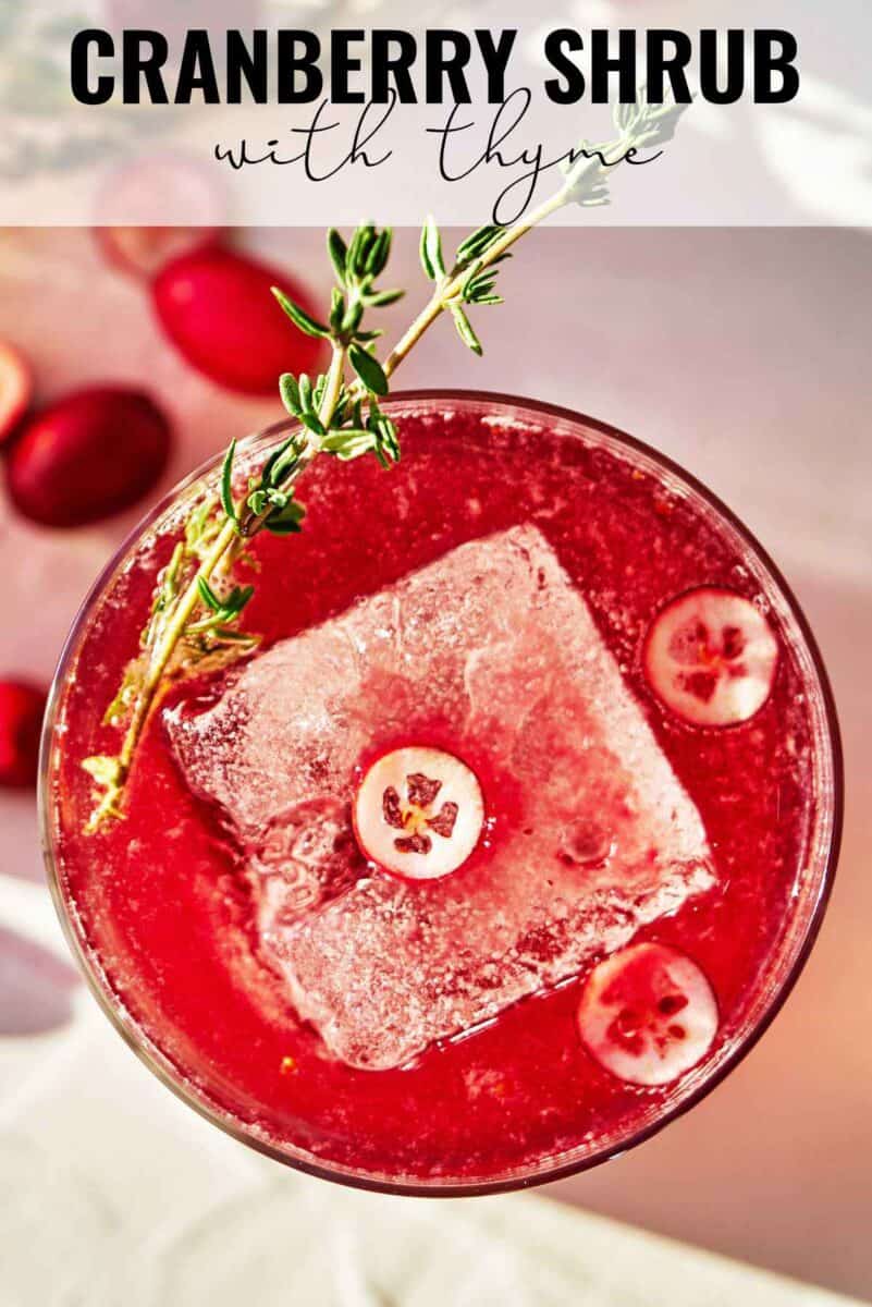 Red drink with a thyme garnish and large ice cube and title text.