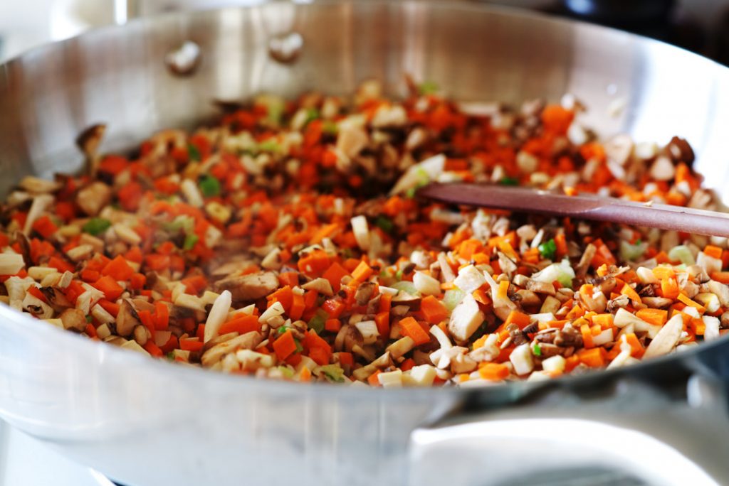 Finely chopped vegetables in a frying pan with wooden spoon.
