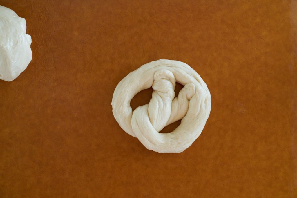 Uncooked pretzel on brown cutting board.