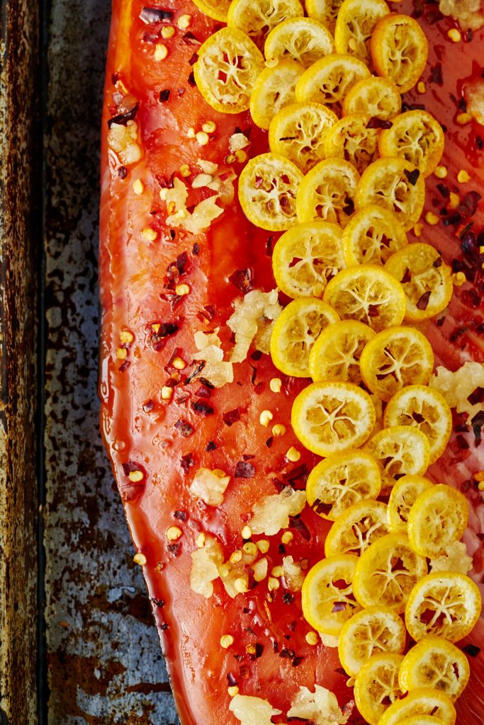 A close up of raw salmon on a baking sheet covered in slices yellow kumquats. 