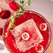 Red beverage with cranberry slices and thyme garnish.