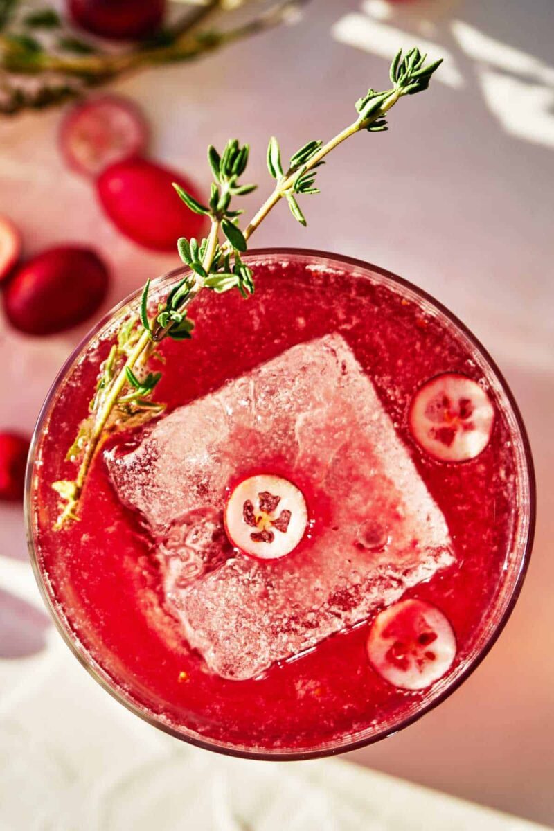 Red beverage with cranberry slices and thyme garnish.