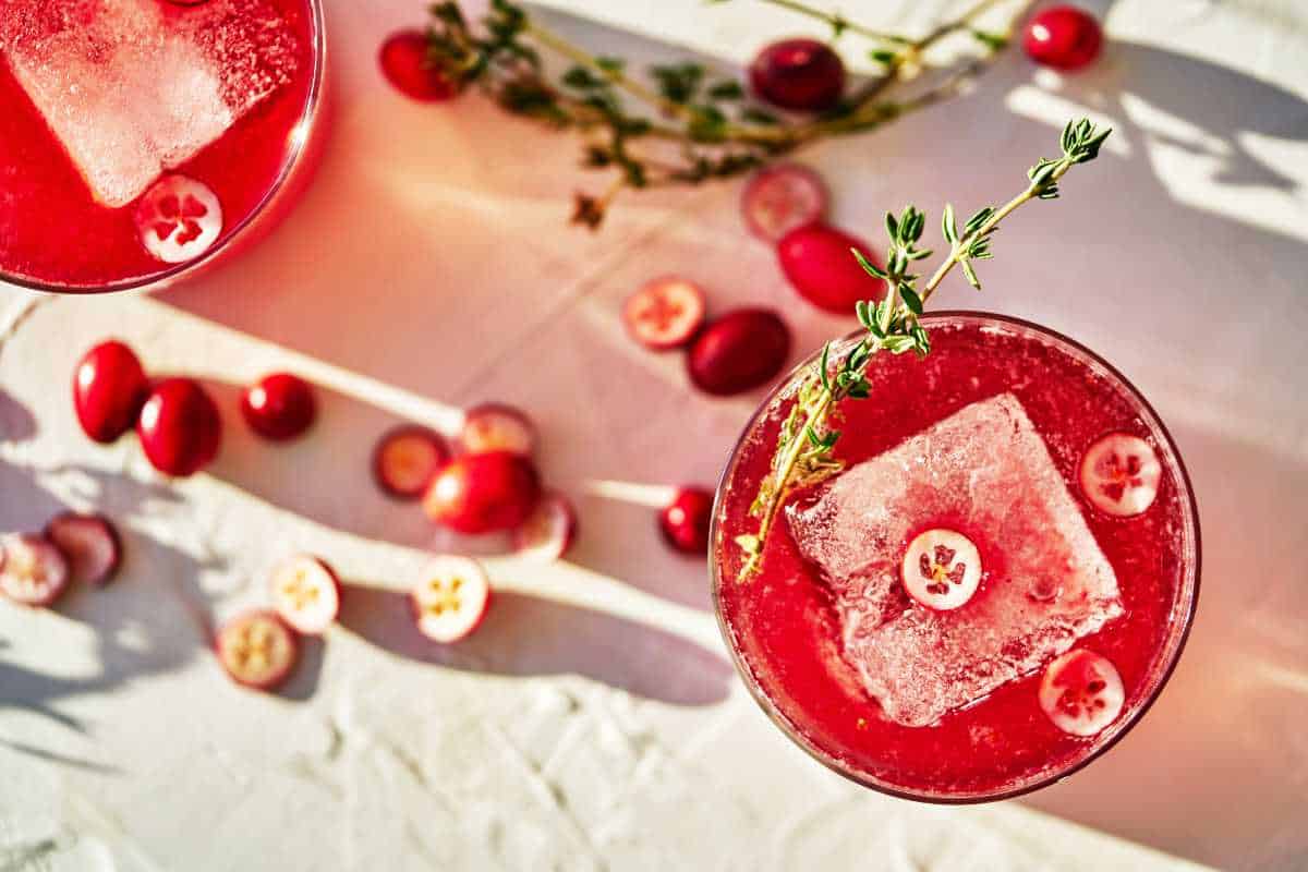 Glass of red drink with a large ice cube and thyme garnish.