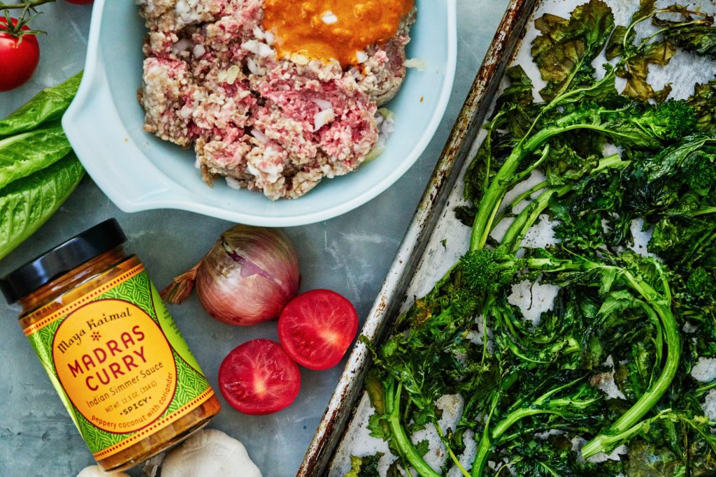 Flat lay of curry sauce, meat and egg in a white bowl, vegetables, and a tray of roasted broccoli.