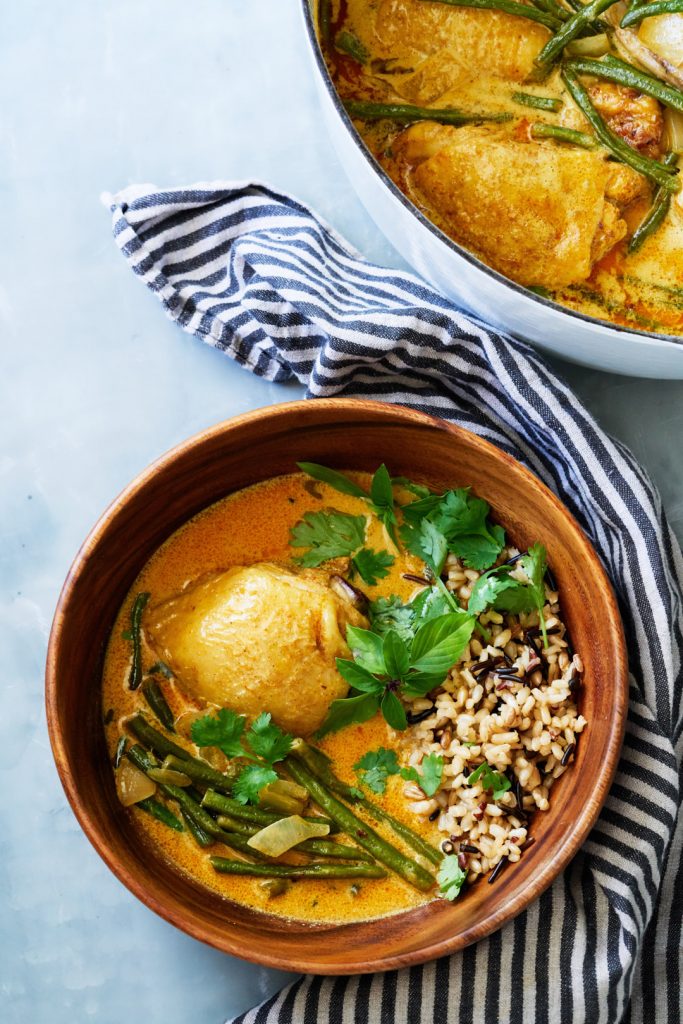 Chicken coconut curry in wooden bowl next to large pot.