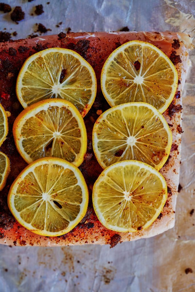 Close up of white fish on parchment paper covered in spices and slices of lemon.