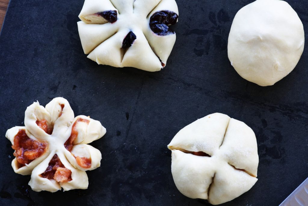 Balls of jam-filled pastry with small cuts into the dough, on a black chopping board.