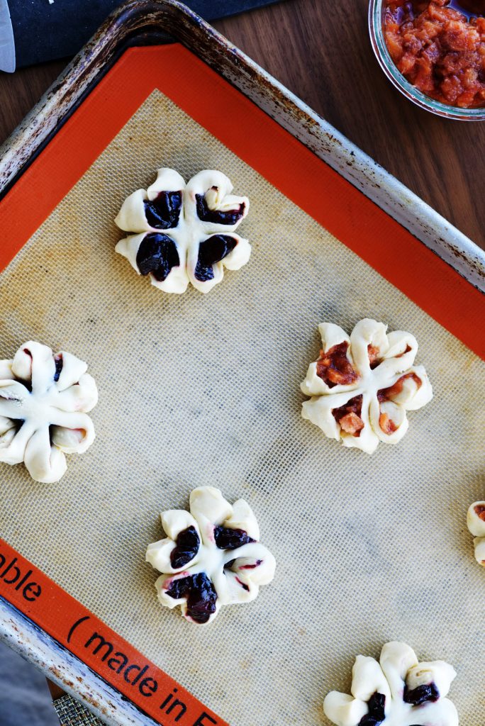 Pastry and jam flowers sitting on a silpat mat on a silver baking sheet.