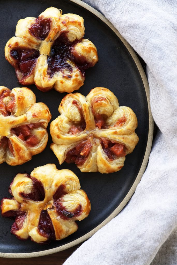 Pastry flowers willed with red and purple jam on a black ceramic plate.