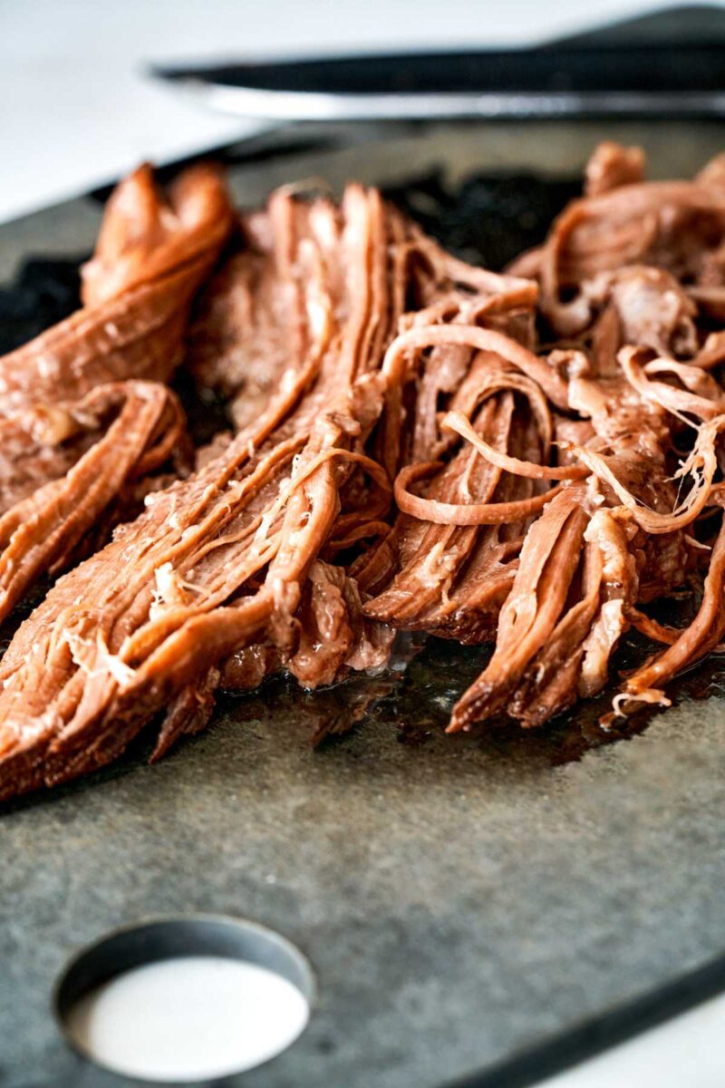 Shredded meat on a black cutting board.