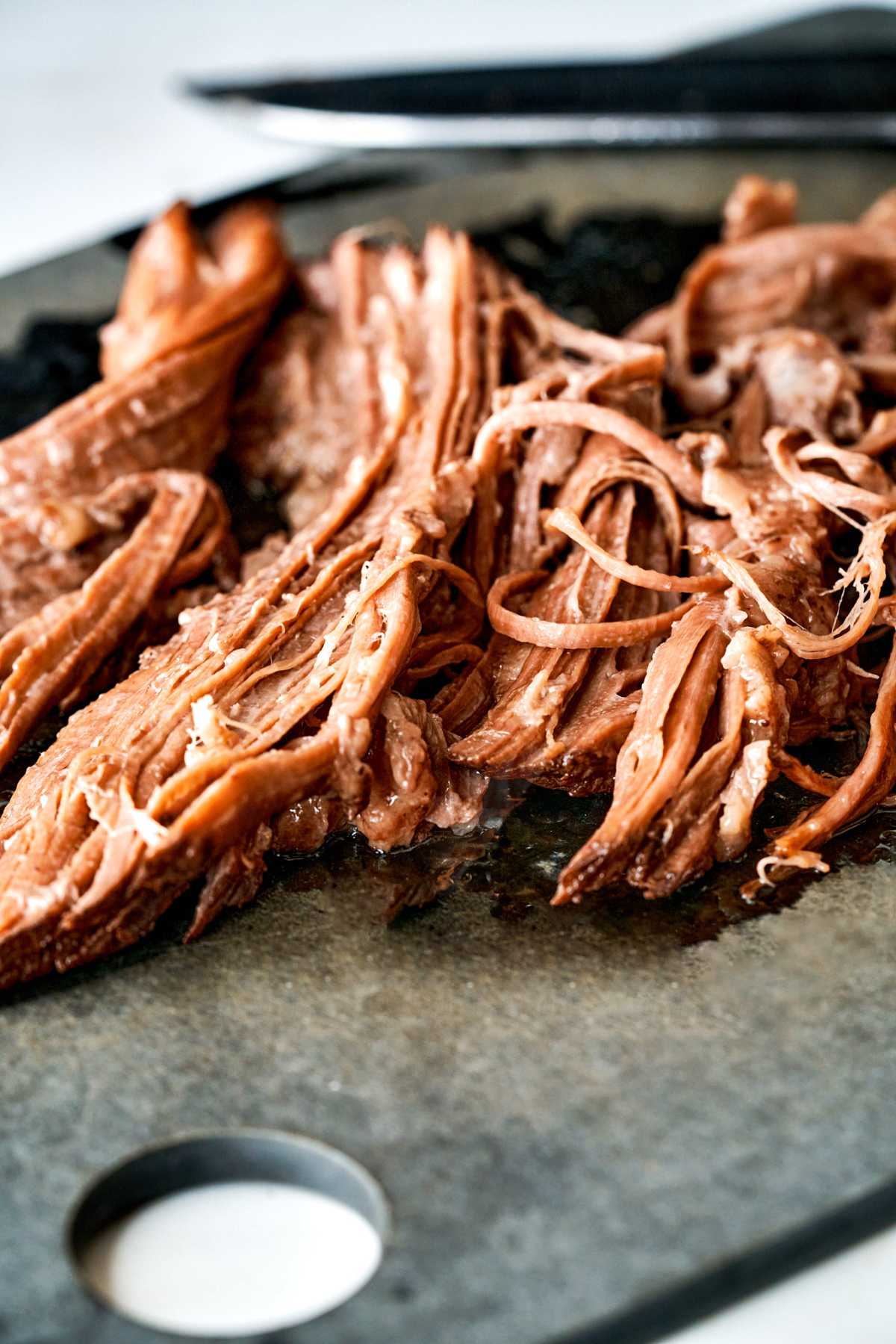 Shredded meat on a black cutting board.