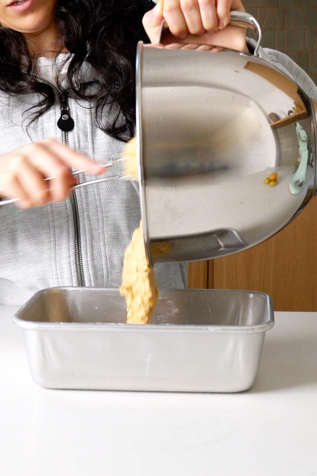 Pouring batter into a loaf pan from a stand mixer bowl.