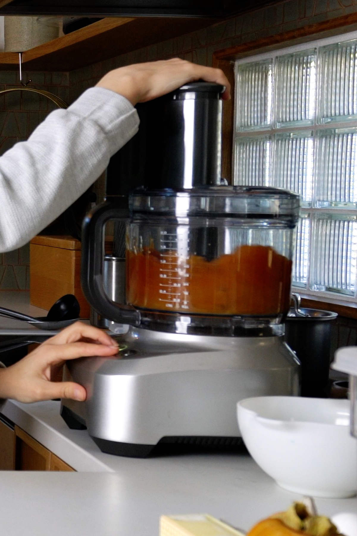 Orange pulp being processed in a food processor next to a window.