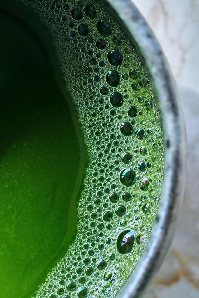 Close up of a bright green drink in a ceramic cup with large and small bubbles at the rim.