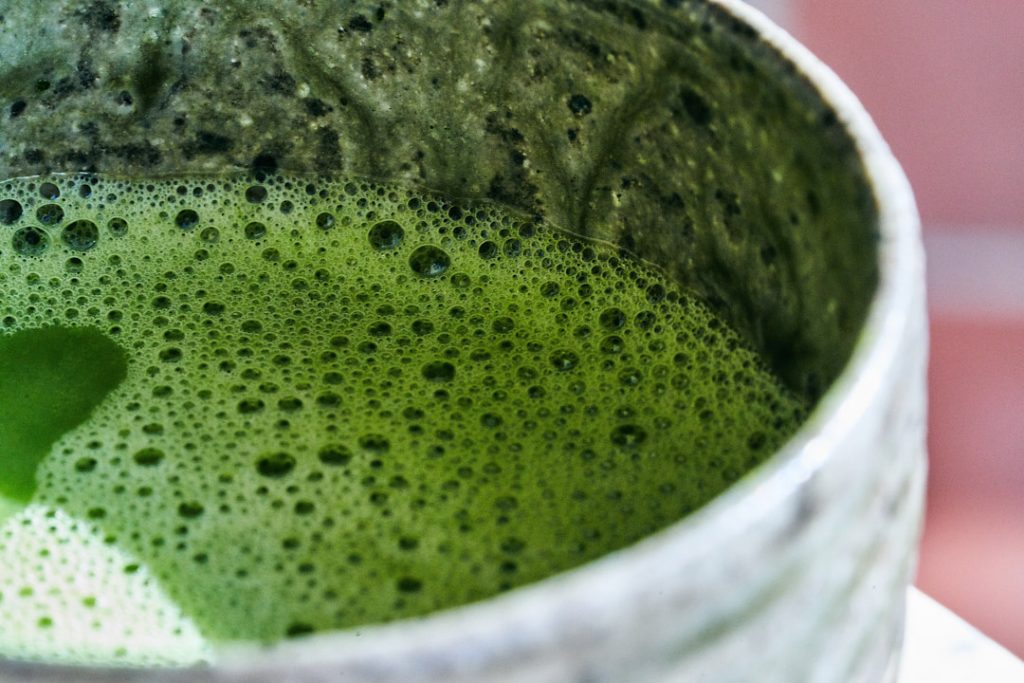 Close up pf a bright green drink with small bubbles in a gray ceramic cup.