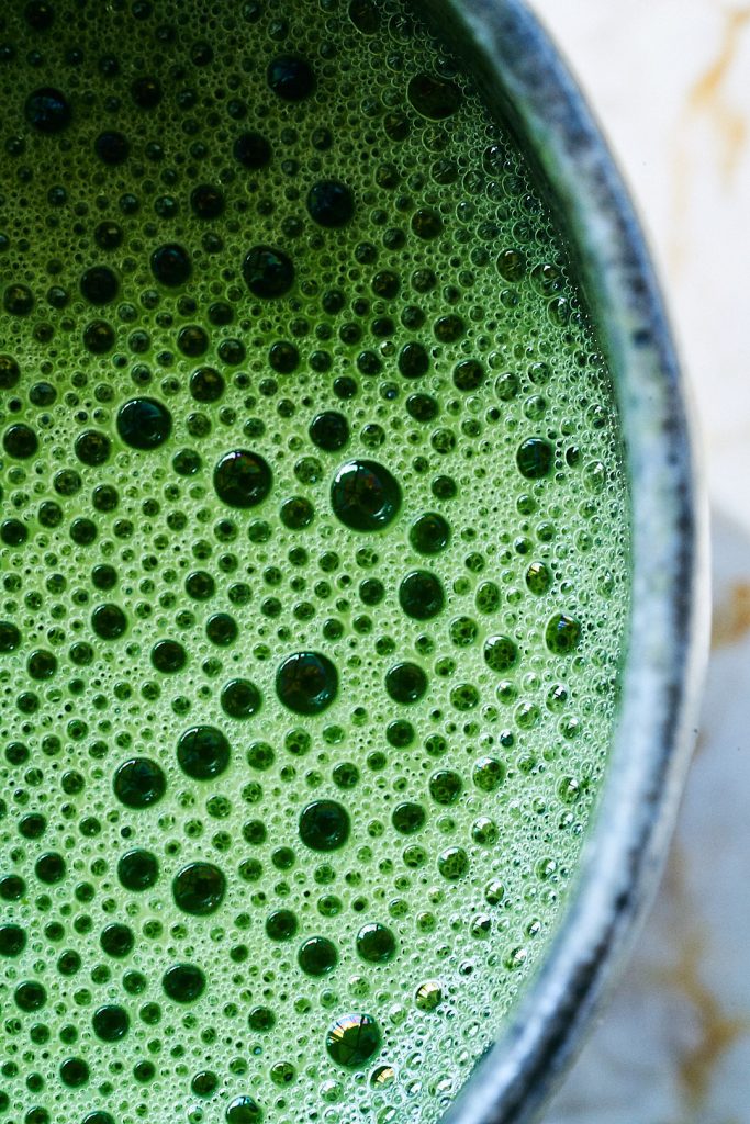 Close up pf a bright green drink with large and small bubbles in a ceramic cup.