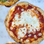 Pizza with red sauce and garlic on white marble.