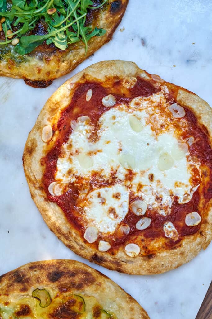 A pizza with red sauce, white cheese, and garlic on a white marble countertop.
