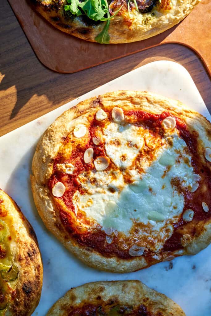 Pizza on a white marble cutting board next to three other pizzas.