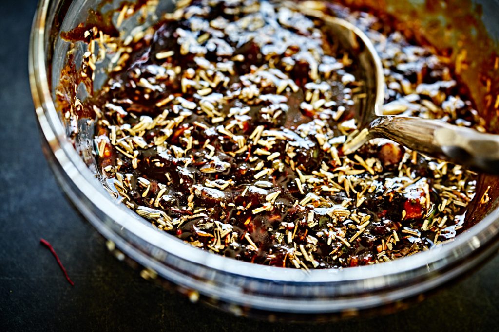 Dark brown marinade with spices in a small glass bowl with a silver spoon.