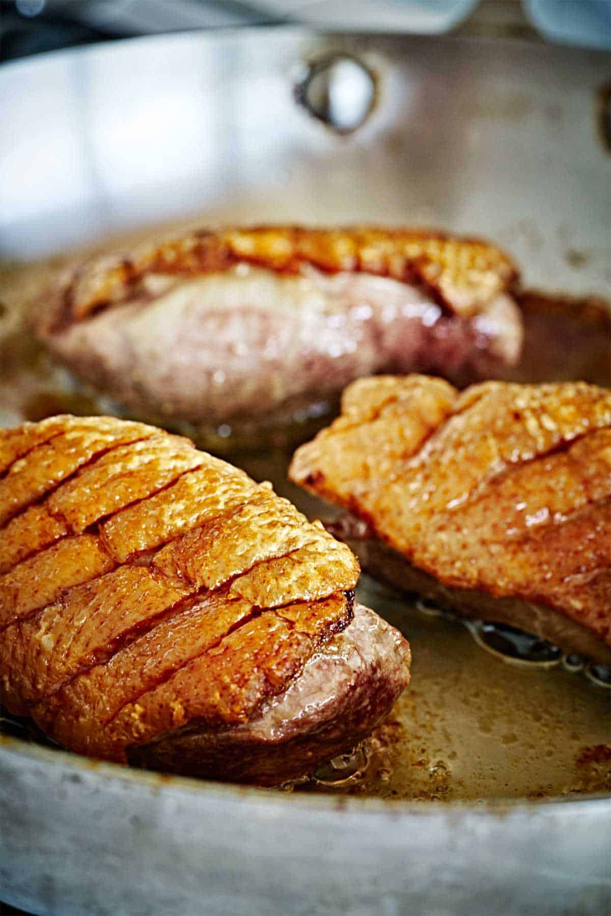 Seared duck breasts in a pan.