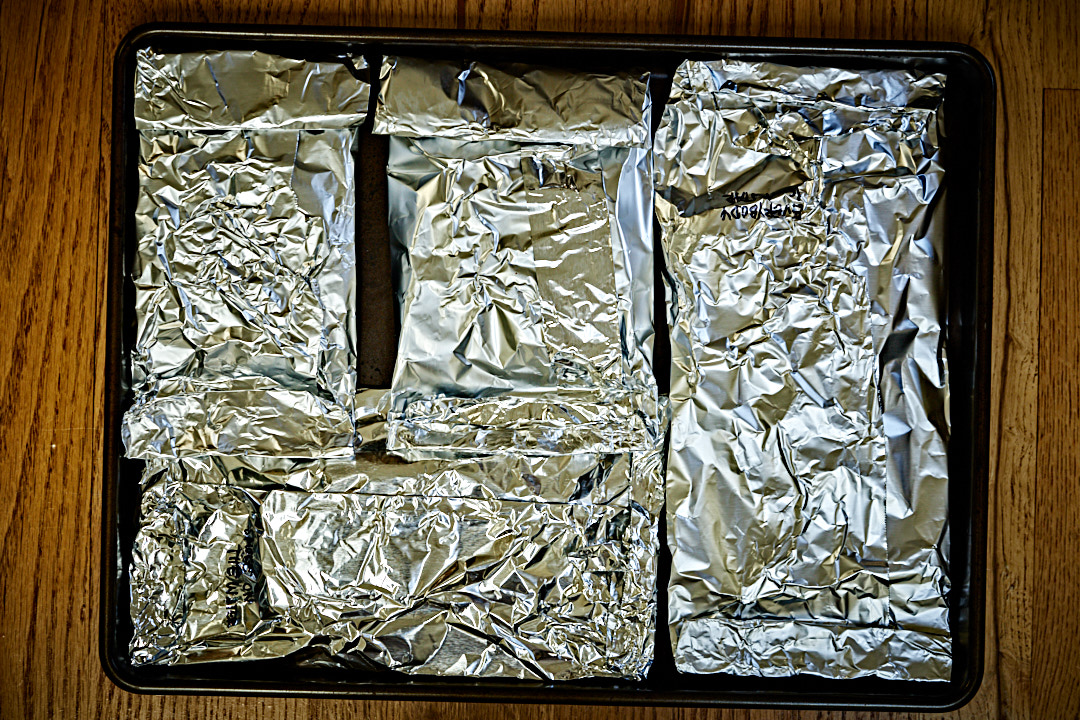 Several small aluminum foil parcels packed onto a baking tray.