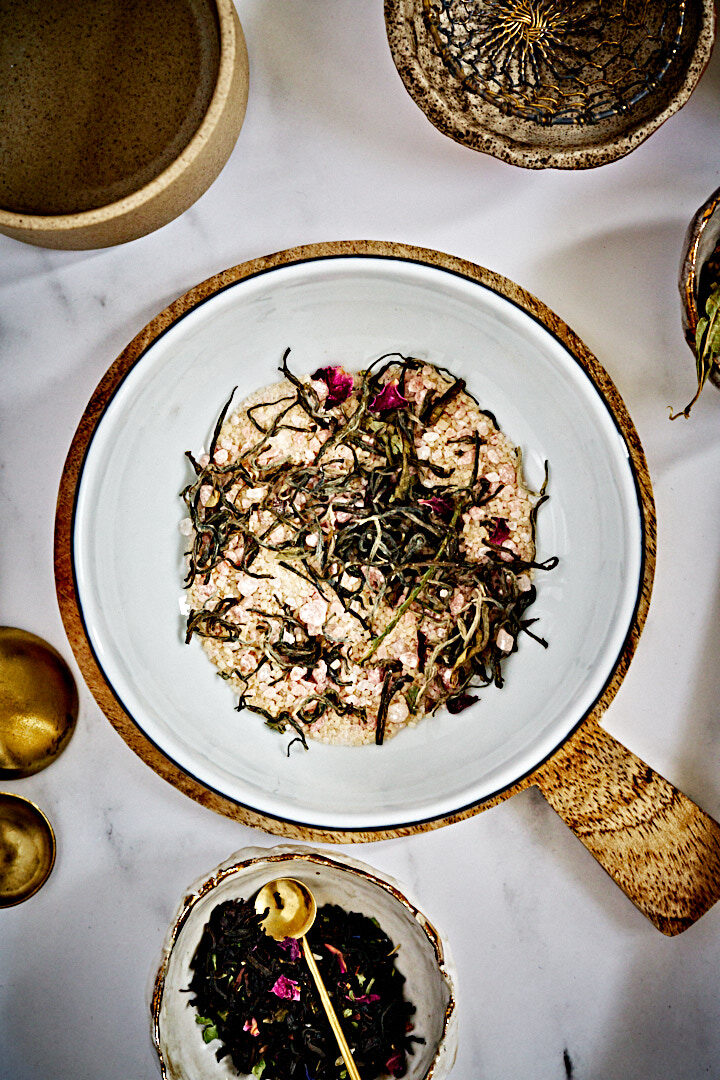 A mixture off tea leaves salt and sugar in a large white bowl surrounded by smaller bowls of tea leaves.