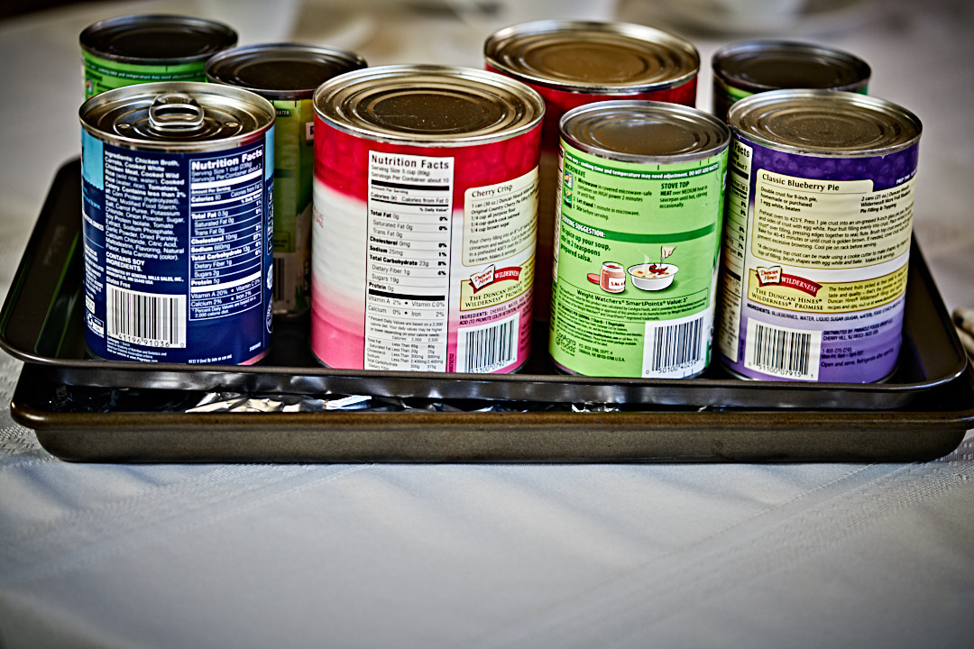 An assortment of cans on a metal baking sheet weighing down fish wrapped in foil.