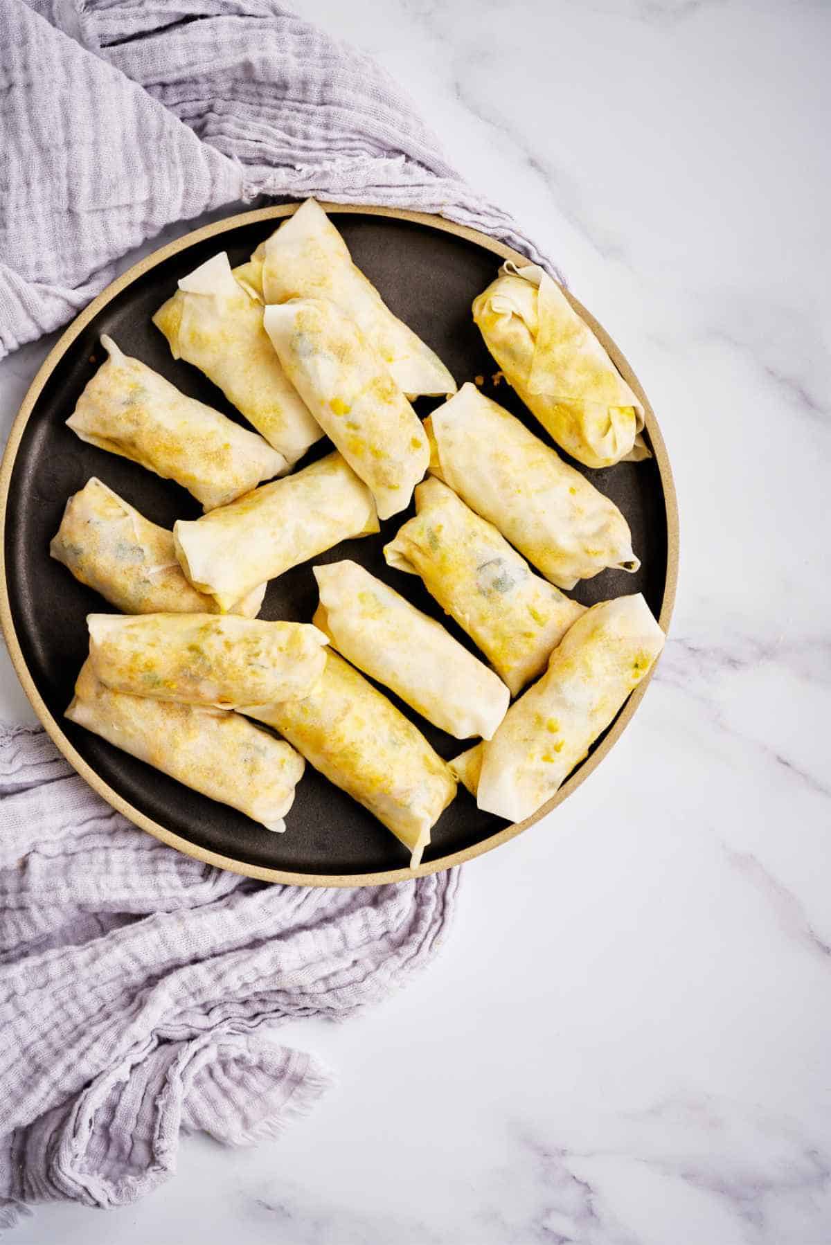 Uncooked egg rolls on a black plate.