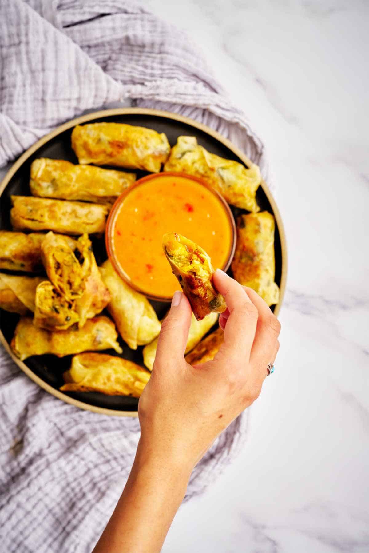 Dipping egg roll into orange sauce.