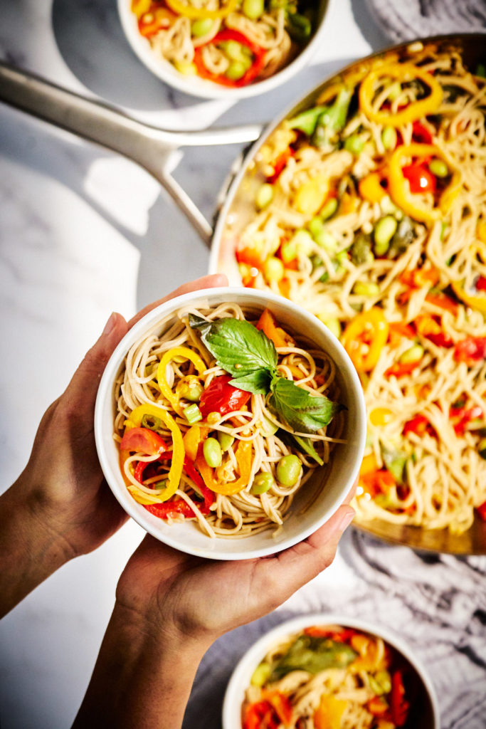 Two hands holding a bowl of soba stir fry.