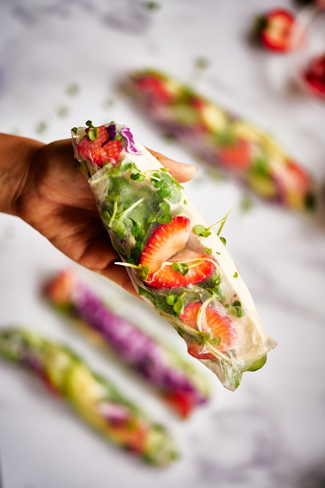 Close up of a hand holding a see through salad roll with tofu, strawberry, and watercress.