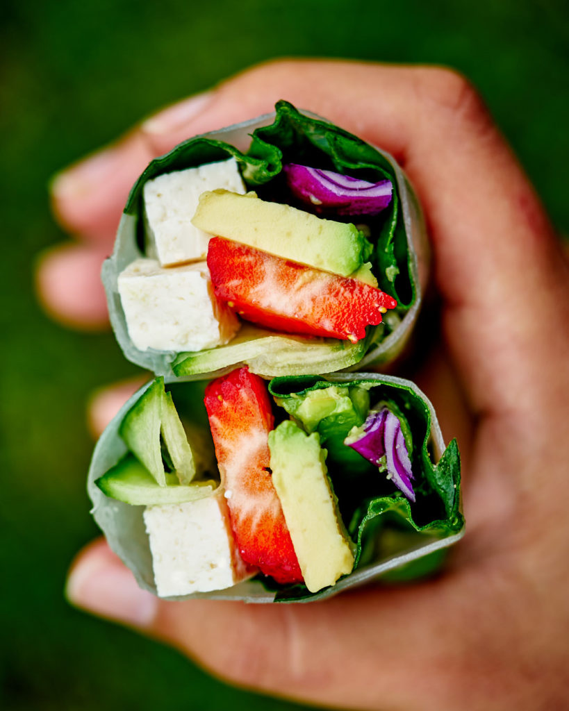 Hand holding two stacked summer salad rolls.
