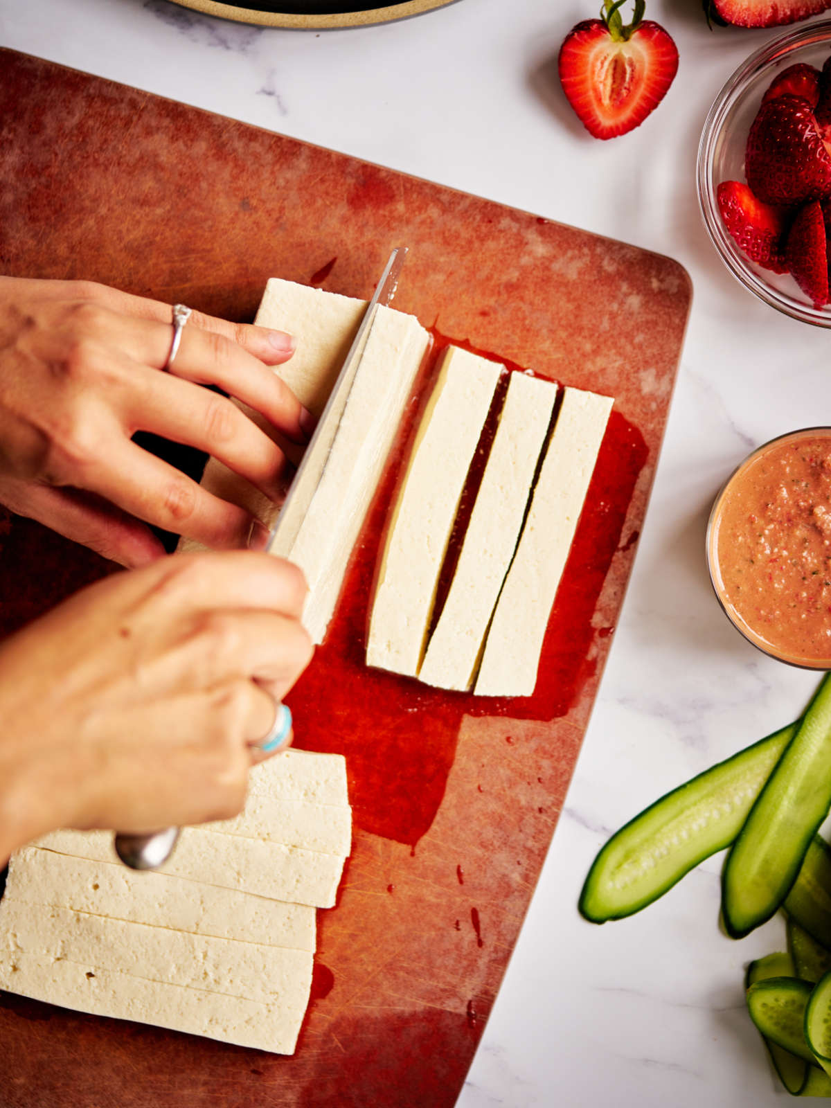 Cutting tofu in strips on a brown cutting board.